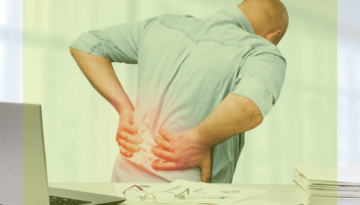 Ein Mann dreht sich vom Schreibtisch weg und stützt sich mit den Händen auf den schmerzenden Rückenbereich. Ein roter Punkt symbolisiert Rückenschmerzen.